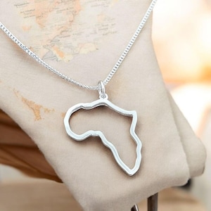 Può includere: Una collana d'argento con un ciondolo a forma di continente africano. Il ciondolo è un contorno dettagliato, sospeso a una catena delicata. La collana è mostrata su uno sfondo neutro.