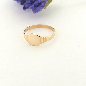 May include: A gold signet ring with a smooth, oval-shaped top. The ring is on a white surface.
