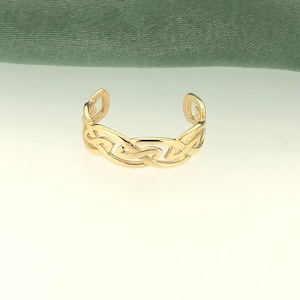 Op de afbeelding: Een gouden ring met een Keltisch knoopontwerp. De ring is gemaakt van glad, gepolijst metaal en heeft een klassieke, tijdloze uitstraling.