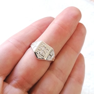 Könnte beinhalten: Ein silberner Siegelring mit einem strukturierten Design auf der Oberseite. Der Ring wird an einem Finger getragen.