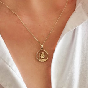 May include: A gold chain necklace with a round pendant featuring a detailed image of a person holding a staff. The pendant is on a delicate chain.