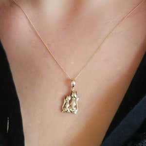 May include: A gold necklace with a pendant featuring two stylised cats facing each other.