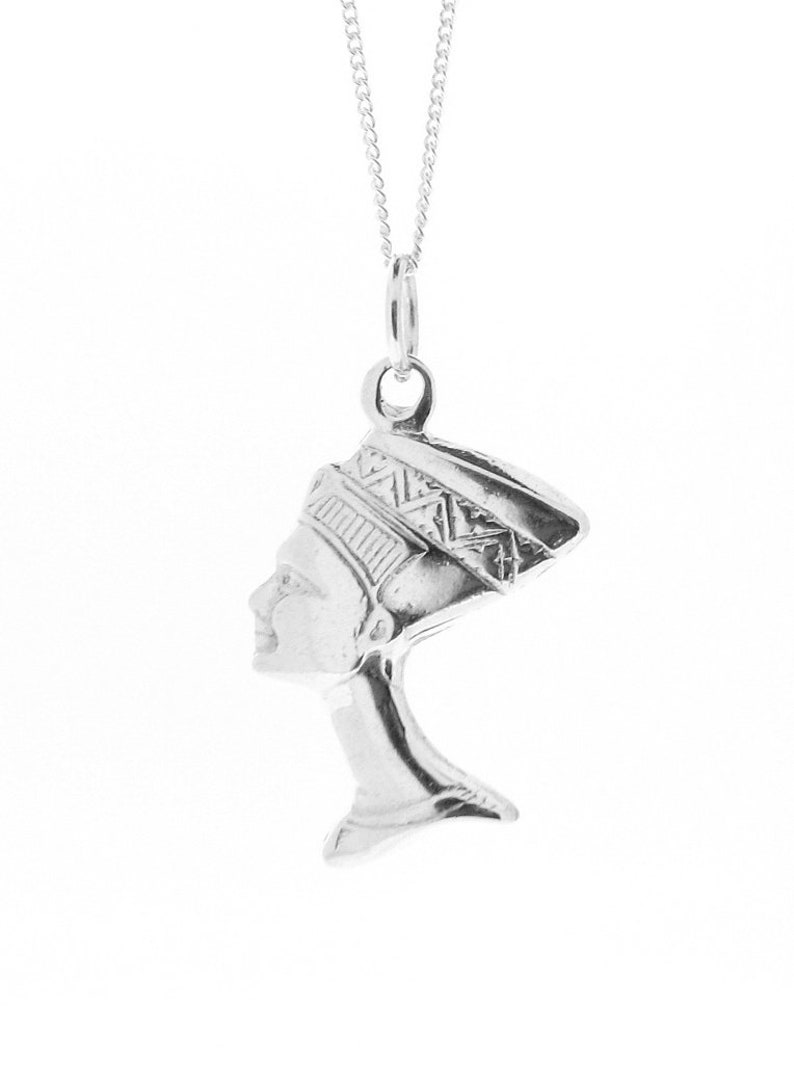 May include: Silver pendant necklace featuring a profile of an Egyptian queen wearing a headdress. The pendant is detailed with intricate patterns and is suspended from a silver chain.