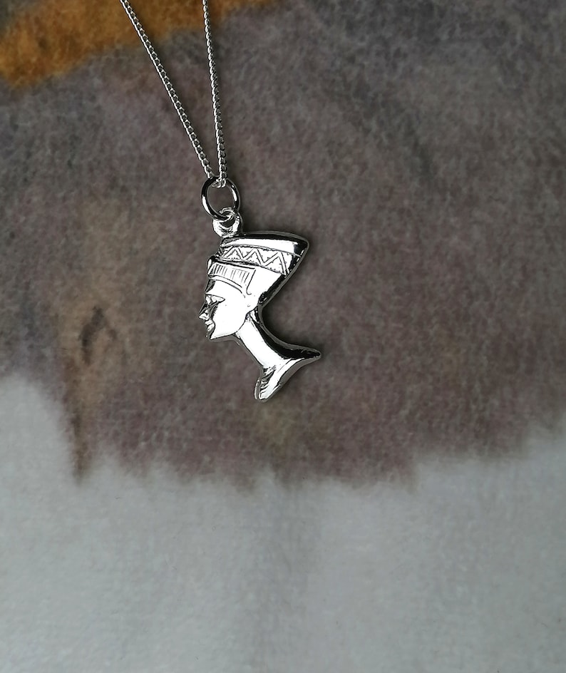 May include: Silver necklace with a pendant of the profile of an Egyptian queen wearing a headdress.