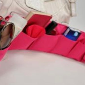 Pu&ograve; includere: Organizzatore in tessuto rosa con pi&ugrave; tasche per una borsa a mano. L'organizzatore ha una tasca per gli occhiali da sole, una tasca per un piccolo taccuino, una tasca per un telefono e una tasca per una bottiglia piccola.