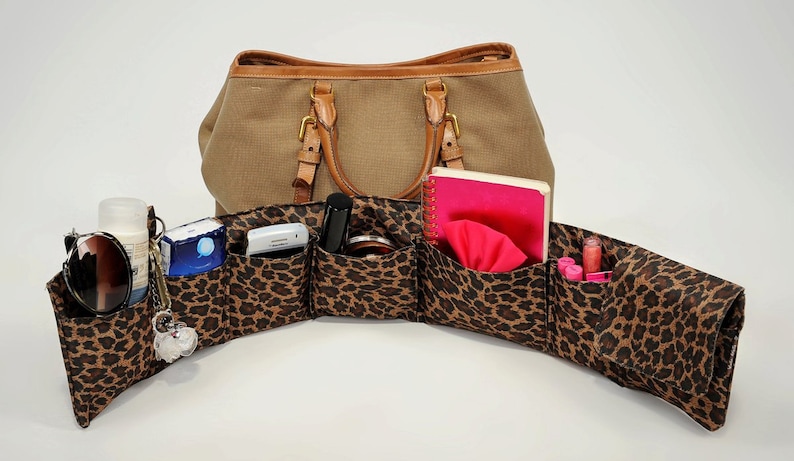 Pu&ograve; includere: Un organizzatore con stampa leopardata con pi&ugrave; tasche per una borsa a mano. L'organizzatore &egrave; pieno di vari oggetti, tra cui occhiali da sole, lozione, un taccuino e trucco.