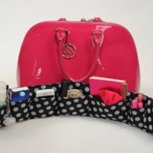 Pu&ograve; includere: Una borsa a mano in pelle verniciata rosa con un inserto organizzatore in tessuto bianco e nero a pois. L'organizzatore ha pi&ugrave; scomparti per riporre piccoli oggetti.