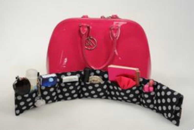 Pu&ograve; includere: Una borsa a mano in pelle verniciata rosa con un inserto organizzatore in tessuto bianco e nero a pois. L'organizzatore ha pi&ugrave; scomparti per riporre piccoli oggetti.