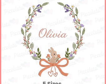 May include: An embroidered floral wreath design with the name "Olivia" in the center. A small bunny sits above a peach-colored bow with two heart-shaped charms. The text "5 Sizes" is at the bottom.