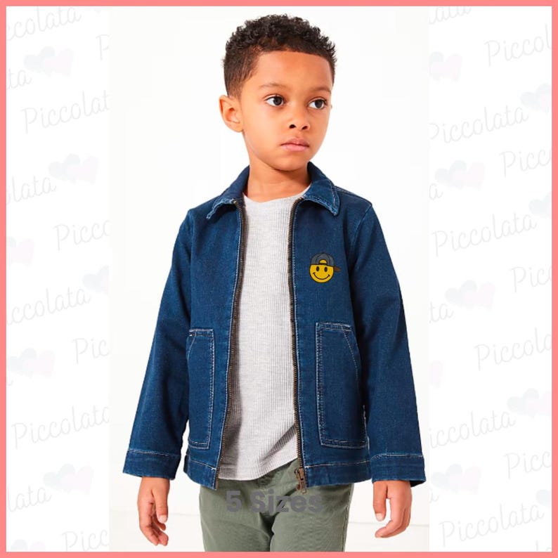 May include: A young boy wearing a blue denim jacket with a yellow smiley face patch. The jacket has a zipper closure and two pockets on the front. The boy is wearing a grey t-shirt and green pants.
