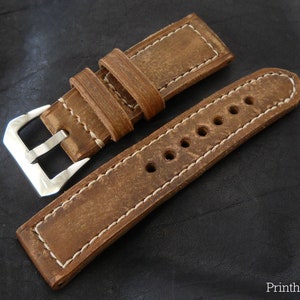Può includere: Un cinturino da orologio in pelle marrone con cuciture bianche e una fibbia argentata. Il cinturino ha più fori per regolare la vestibilità.