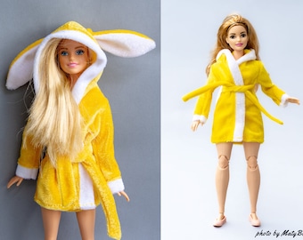 May include: A yellow plush bathrobe with white trim and bunny ears. The robe is worn by a doll with long blonde hair.
