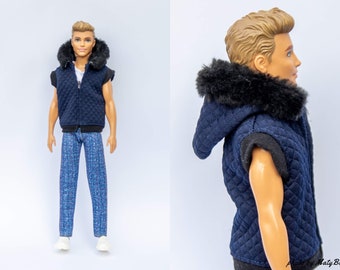 Könnte beinhalten: Eine blaue gesteppte Weste mit einer schwarzen Kapuze mit Kunstfellfutter. Die Weste hat einen Reißverschluss und ist ärmellos. Die Weste wird von einer Puppe mit blonden Haaren getragen.