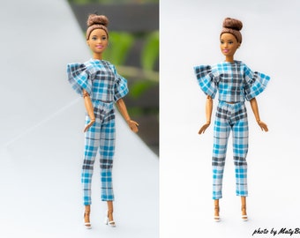 May include: A doll wearing a blue, gray, and white plaid crop top with ruffled sleeves and matching pants. The doll has brown hair and is wearing white high-heeled shoes. The outfit is a miniature version of a modern fashion ensemble.