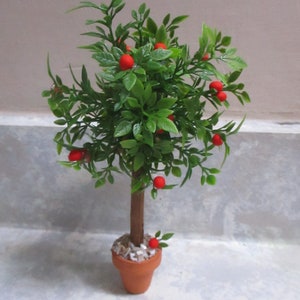 May include: A small potted artificial tree with green leaves and red fruit. The tree is in a brown terracotta pot with white gravel.