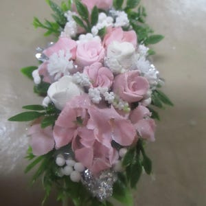 May include: A small bouquet of pink and white fabric flowers with green leaves and silver glitter accents.