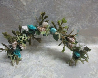 May include: A green, white, and blue floral crown with seashells and beads. The crown is made of artificial flowers and is perfect for a beach wedding or a summer party.