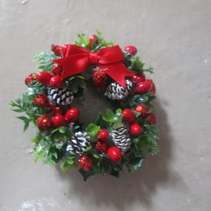 May include: A small Christmas wreath with red berries, pine cones, and a red bow.