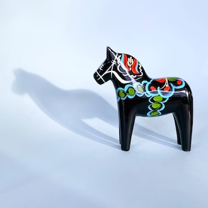 Pode incluir: Um cavalo Dala de madeira preto com desenhos pintados coloridos. O cavalo tem um padrão floral azul, verde, vermelho e branco.