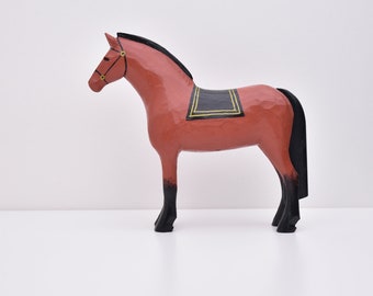 Puede incluir: Una figurita de caballo de madera con cuerpo rojo, patas negras y una silla de montar negra con ribetes dorados. El caballo tiene una crin y una cola negras.