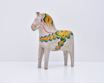 Puede incluir: Un caballo Dala de madera blanco con detalles pintados en amarillo, naranja y verde. El caballo es un juguete tradicional de arte popular sueco.