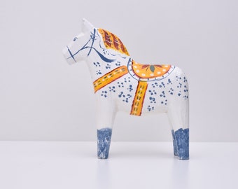 Könnte beinhalten: Eine weiße Holzpferdefigur mit blauen und gelben Maldetails. Das Pferd hat einen Sattel mit einem gelben, orangefarbenen und grünen Blumendesign.