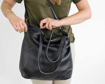 May include: A black leather hobo bag featuring a top zipper closure with a brass-toned metal zipper, two fixed shoulder straps, and an adjustable crossbody strap attached with brass-toned hardware clips on the sides of the bag.