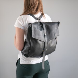 Könnte beinhalten: Ein schwarzer Lederrucksack mit Klappenverschluss und verstellbaren Trägern. Der Rucksack hat ein minimalistisches Design und ist aus hochwertigem Leder gefertigt.