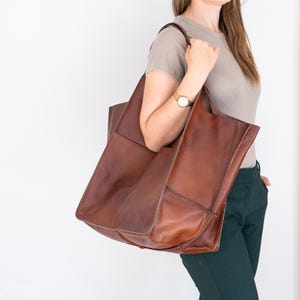 May include: A large brown leather tote bag with a single strap. The bag has a spacious interior and is perfect for carrying everyday essentials.
