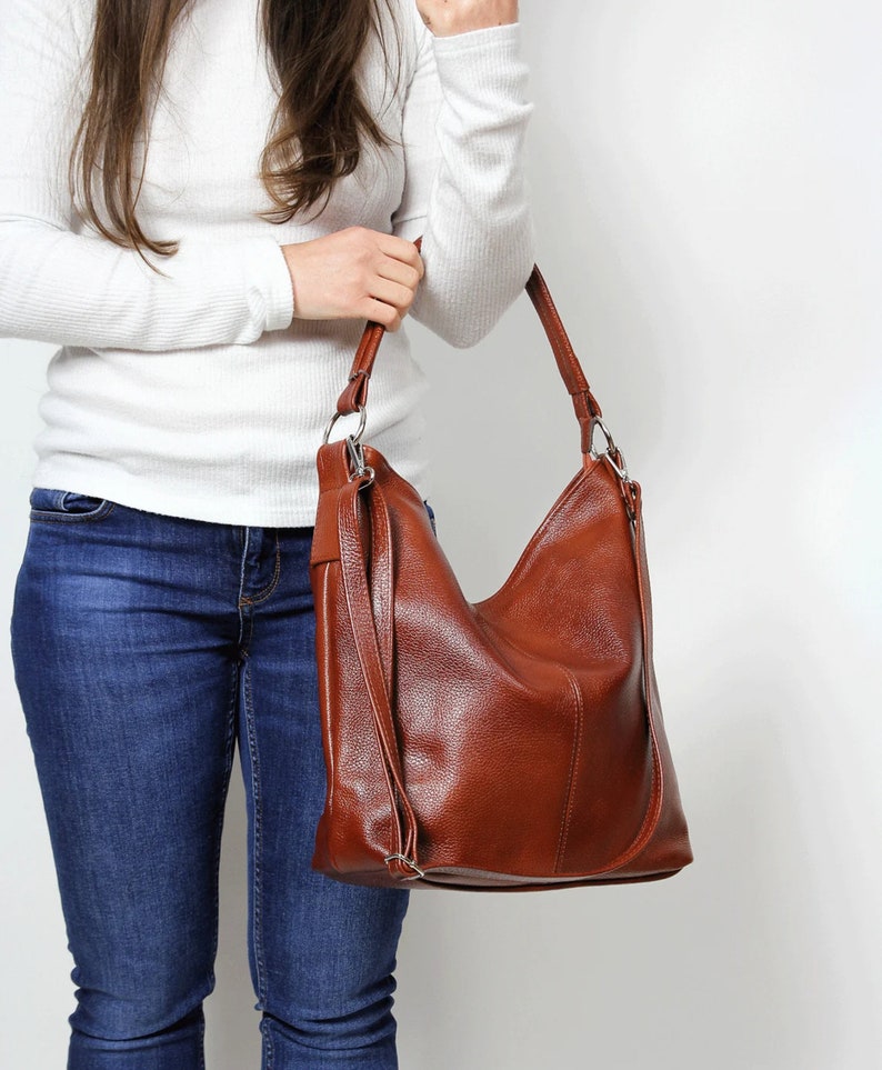 May include: A brown leather hobo bag with a long strap. The bag has a flap closure and a zippered pocket on the front.