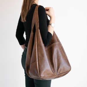 K&ouml;nnte beinhalten: Eine gro&szlig;e braune Ledertasche mit einer breiten &Ouml;ffnung und einem einzigen Trageriemen. Die Tasche hat ein ger&auml;umiges Innenleben und einen l&auml;ssigen, entspannten Stil.