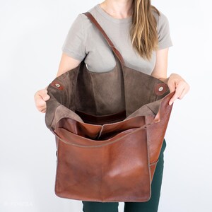 May include: A large brown leather tote bag with a brown suede lining. The bag is open and the lining is visible. The bag has a single strap and a zippered pocket on the front.
