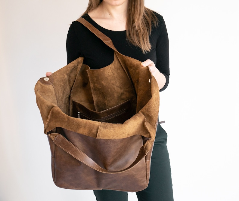 K&ouml;nnte beinhalten: Eine braune Ledertasche mit einem Futter aus Wildleder. Die Tasche ist offen und das Futter ist sichtbar. Die Tasche hat einen einzigen Riemen und eine Rei&szlig;verschlusstasche im Inneren.