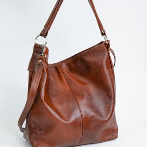 May include: A brown leather tote bag with a single strap. The bag has a simple design and is made of high-quality leather.