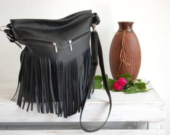 May include: A black shoulder bag featuring long fringe detailing along the front panel. The bag includes two horizontal zippered pockets with silver-toned hardware and a matching adjustable shoulder strap attached with metal rings.
