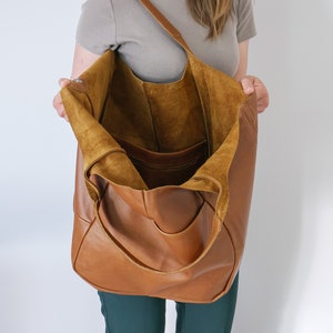 K&ouml;nnte beinhalten: Eine gro&szlig;e, unstrukturierte Hobo-Tasche aus braunem Leder mit einem breiten Schulterriemen. Das Innere ist ungef&uuml;ttert, zeigt die nat&uuml;rliche Wildlederstruktur des Leders und verf&uuml;gt &uuml;ber ein einzelnes Innenfach mit Rei&szlig;verschluss.