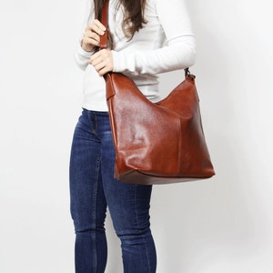 May include: A brown leather shoulder bag with a slouchy design. The bag has a long strap and is worn over the shoulder.