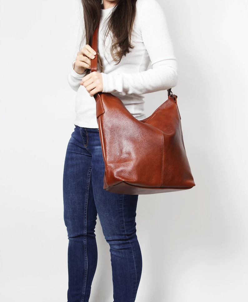 May include: A brown leather shoulder bag with a slouchy design. The bag has a long strap and is worn over the shoulder.