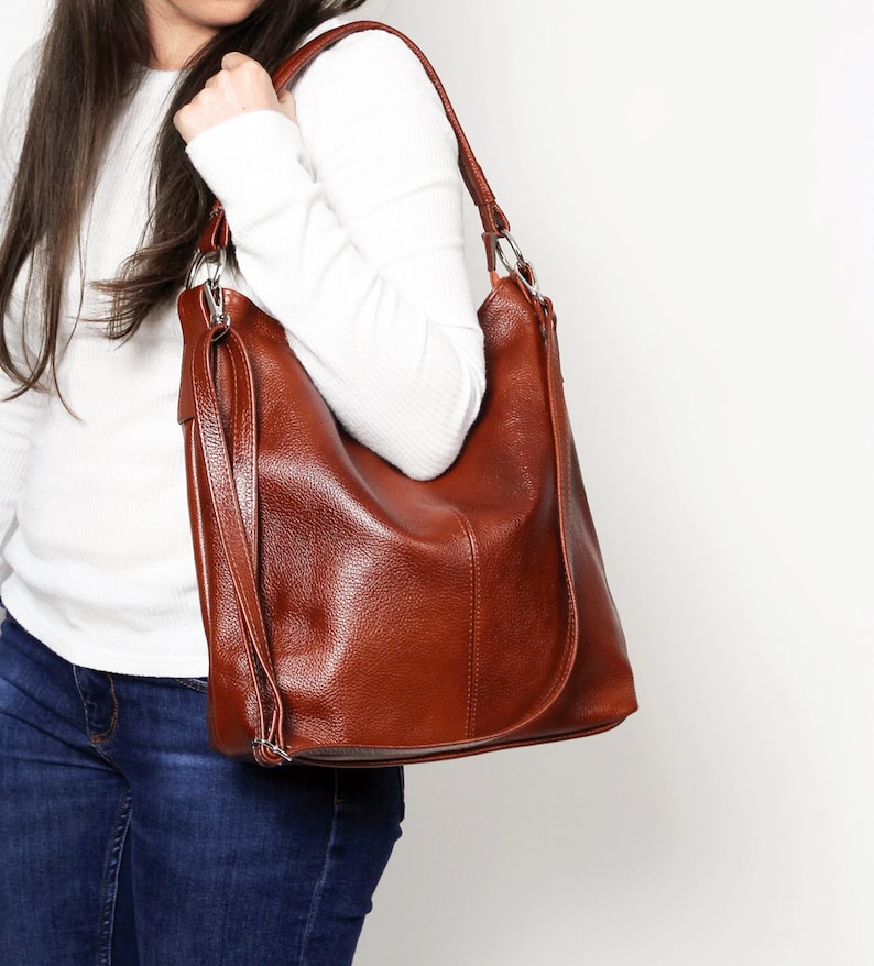 May include: A brown leather shoulder bag with a long strap. The bag has a slouchy, casual look and is made of a soft, supple leather.