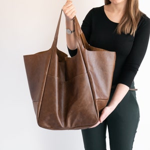 K&ouml;nnte beinhalten: Eine gro&szlig;e braune Ledertasche mit einer breiten &Ouml;ffnung und einem einzigen Henkel. Die Tasche ist aus weichem, geschmeidigem Leder gefertigt und hat einen l&auml;ssigen, entspannten Look.