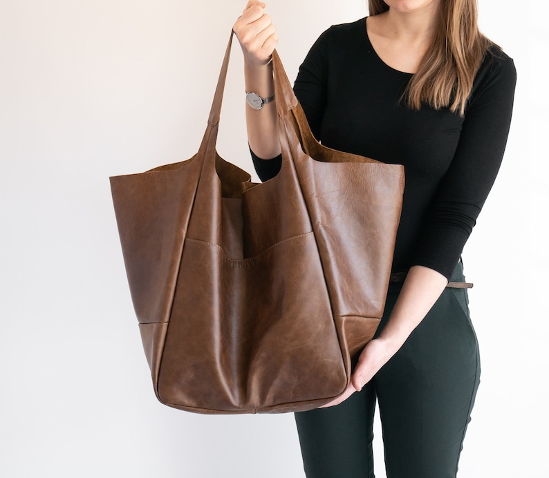 K&ouml;nnte beinhalten: Eine gro&szlig;e braune Ledertasche mit einer breiten &Ouml;ffnung und einem einzigen Henkel. Die Tasche ist aus weichem, geschmeidigem Leder gefertigt und hat einen l&auml;ssigen, entspannten Look.