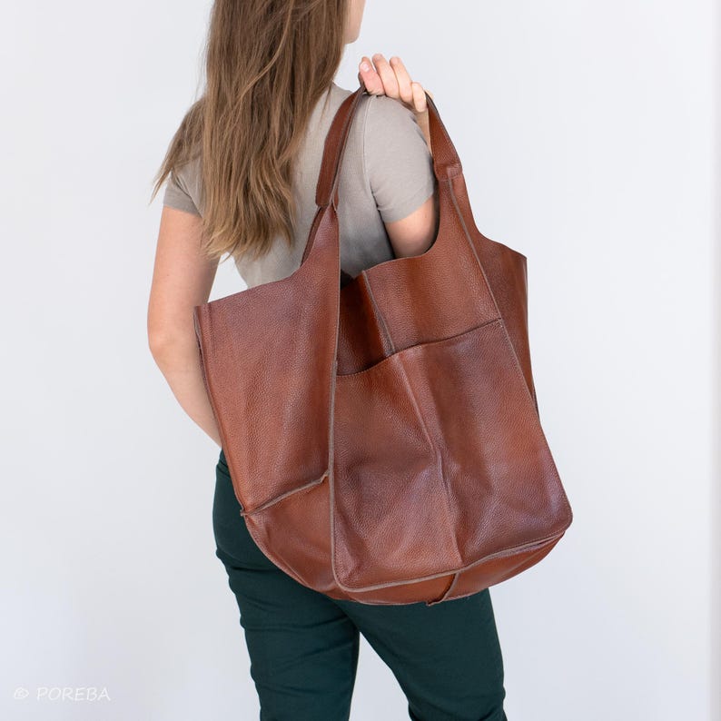 May include: A large brown leather tote bag with multiple pockets. The bag is worn over the shoulder of a person.