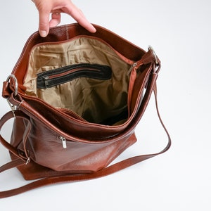 May include: A brown leather shoulder bag with a zippered pocket on the inside. The bag has a long strap and is open, showing the interior lining.