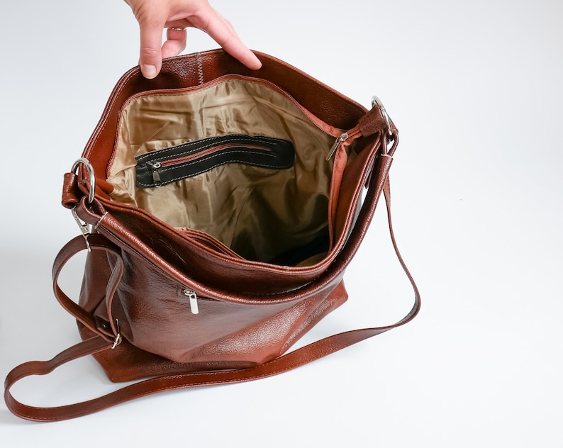 May include: A brown leather shoulder bag with a zippered pocket on the inside. The bag has a long strap and is open, showing the interior lining.