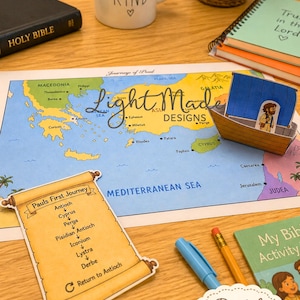 May include: A colorful map with the text "Journeys of Paul" and a paper boat craft. The map shows locations like Antioch and Cyprus. A scroll lists Paul's first journey. The image also includes a Bible, a mug, and a notebook.