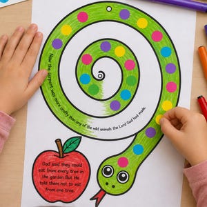 May include: A green, spiral-shaped snake coloring page with colorful dot stickers. The page includes text about the serpent and an apple illustration. Markers and stickers are visible.