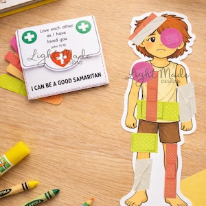 May include: A printable Good Samaritan craft showing a paper figure with bandages and a first aid kit. The kit reads "Love each other as I have loved you, John 15:12" and "I can be a good Samaritan". Crayola crayons and scissors are also visible.