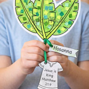 May include: A handmade paper craft featuring three green leaves with colorful mosaic-like details. The craft includes a banner that says "Hosanna" and a paper shirt with the text "Jesus is King Matthew 21:9".