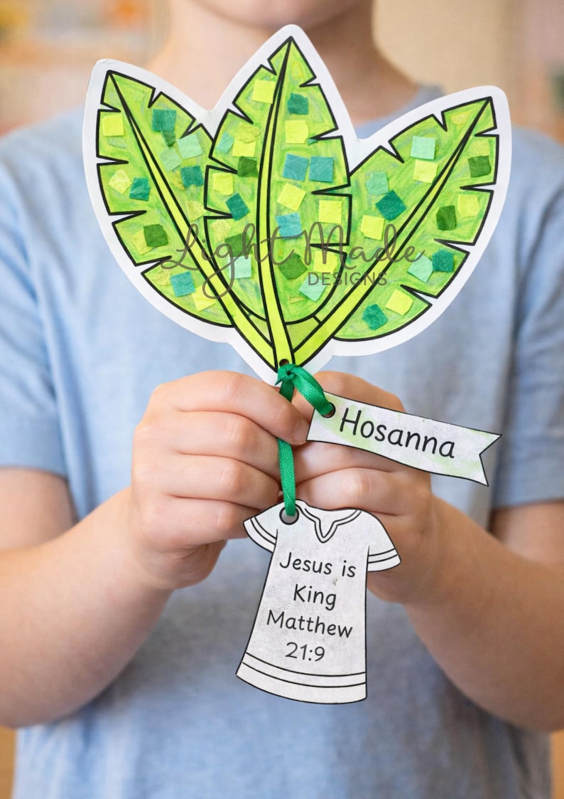 May include: A handmade paper craft featuring three green leaves with colorful mosaic-like details. The craft includes a banner that says "Hosanna" and a paper shirt with the text "Jesus is King Matthew 21:9".