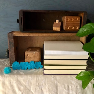 Puede incluir: Una pila de libros con una caja de madera en la parte superior. La caja contiene una pequeña casa de madera y un dado de madera. Una palabra de fieltro azul "Grown" está delante de los libros.
